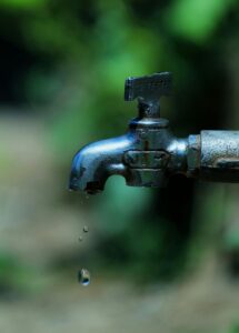 Close-up of an old rusty faucet with water droplets falling against a blurred background.