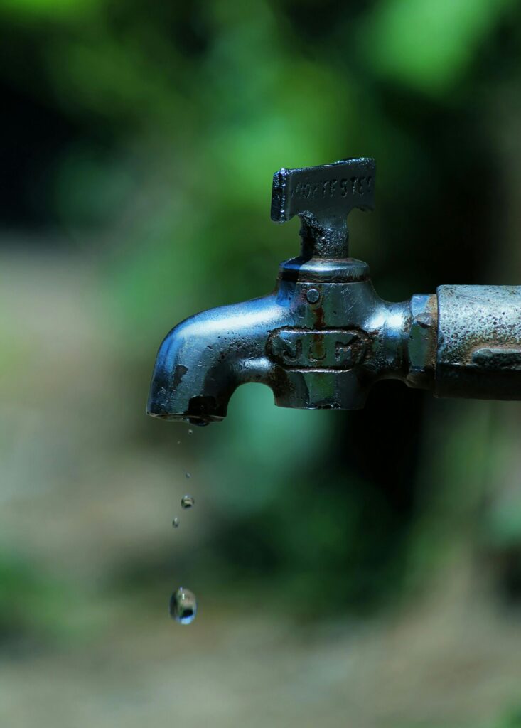 Close-up of an old rusty faucet with water droplets falling against a blurred background.